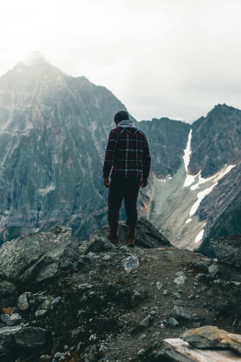 A lone hiker in a plaid jacket stands on a rocky outcrop in the Canadian Rockies.