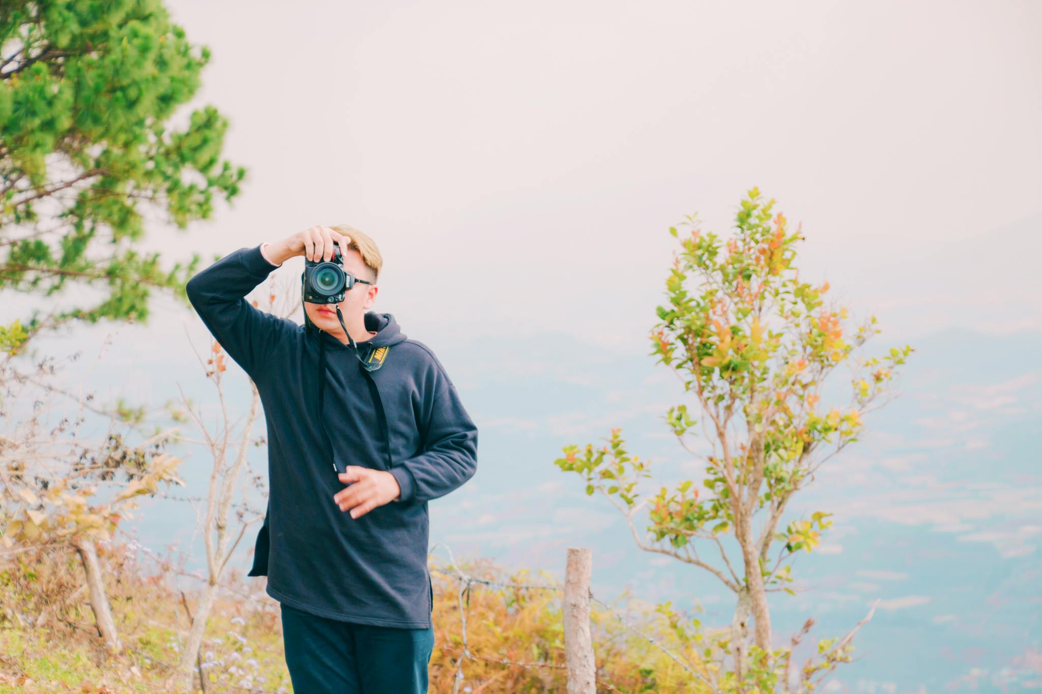 A young man takes photos amidst vibrant nature on a mountainside, showcasing dynamic outdoor photography.