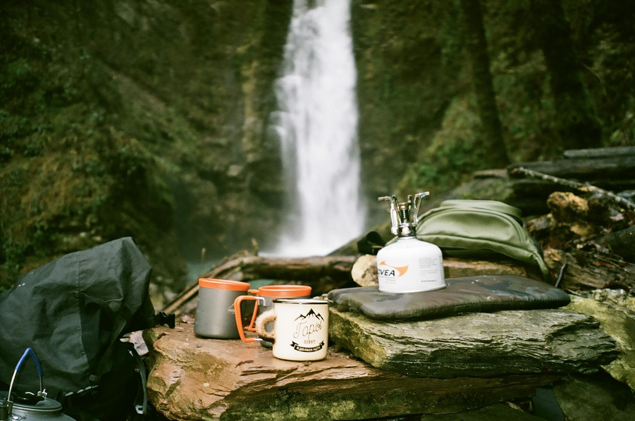 Camping gear set up near a waterfall, showcasing outdoor adventure essentials.