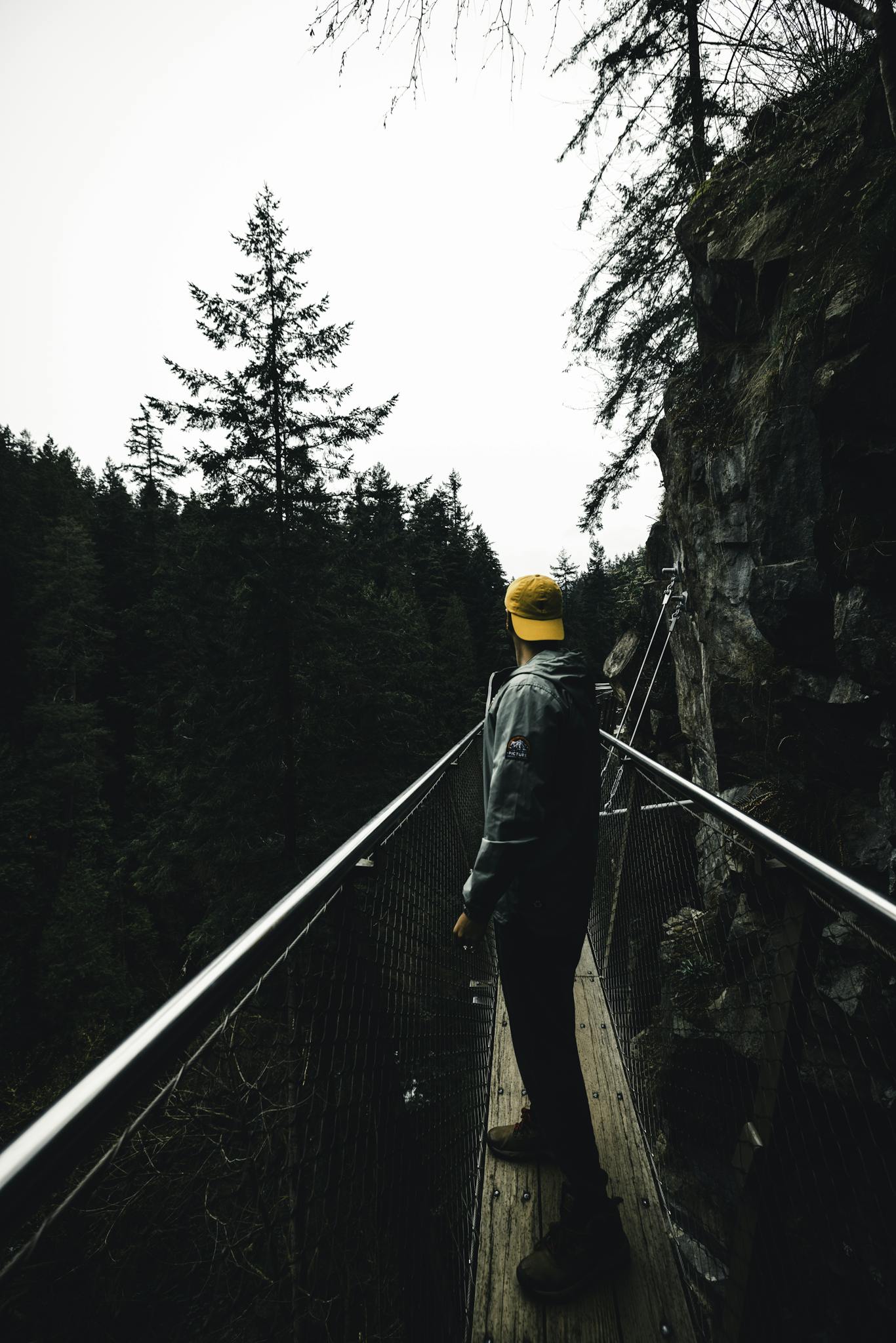 Hiker explores a cliffside suspension bridge amidst Vancouver's lush forest scene.